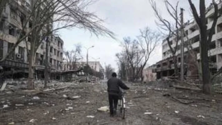 Seorang pria berjalan dengan sepeda di jalan yang rusak akibat penembakan di Mariupol, Ukraina pada 10 Maret 2022. (Foto: AP/Evgeniy Maloletka).