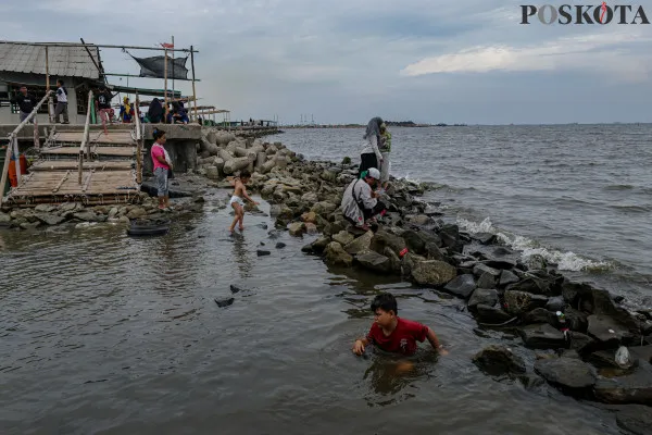 Sejumlah warga menikmati suasana pantai dengan berbagai aktivitas seperti berjalan di sisi pantai, berfoto hingga berenang di tengah banjir rob yang masih melanda di kawasan Pantai Marunda, Jakarta Utara, Kamis, 26 Desember 2024. (Poskota/ Ahmad Tri Hawaari)