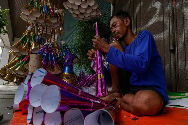 Pengrajin sekaligus pedagang saat menyelesaikan pembuatan terompet kertas sembari menunggu pembeli di Jalan Pintu Besar Selatan, Pancoran Glodok, Jakarta Barat, Jumat, 27 Desember 2024. (Poskota/ Ahmad Tri Hawaari)