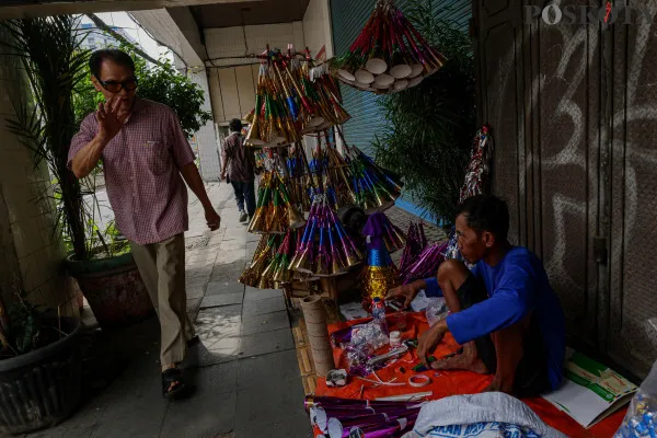 Pengrajin sekaligus pedagang saat menyelesaikan pembuatan terompet kertas sembari menunggu pembeli di Jalan Pintu Besar Selatan, Pancoran Glodok, Jakarta Barat, Jumat, 27 Desember 2024. (Poskota/ Ahmad Tri Hawaari)