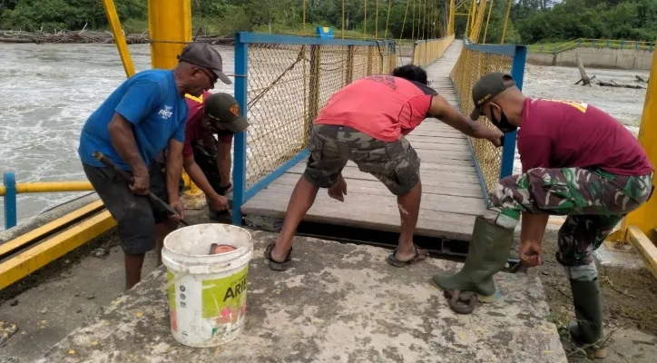 Prajurit TNI membantu perbaiki jembatan gantung yang rusak akibat banjir. (foto: ist)