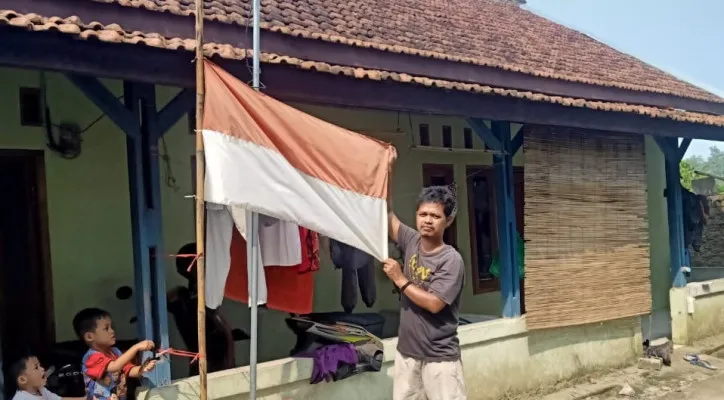 Abdul Kohar,  salah seorang warga, mengibarkan bendera merah putih setengah tiang. (foto: ist)