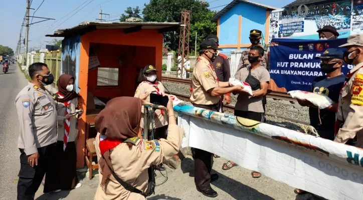 Kasat Binmas Polres Metro Depok mendampingi Saka Bhayangkara Depok membagikan bansos paket beras kepada penjaga pintu tanpa palang sepanjang Jalan Raya Citayam. (Foto/Poskota.co.id/Angga)