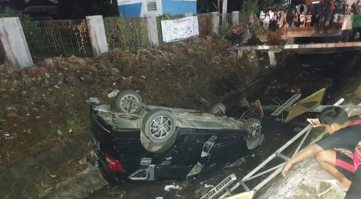 Kondisi kendaraan Datsun Go yang terbalik dalam saluran irigasi menjadi tontonan warga. (Foto: Rahmat Haryono)