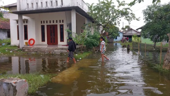 Foto : Dua orang anak sedang melintas dihalaman rumah menerjang genangan air di Tarumajaya, Bekasi. (Ist)