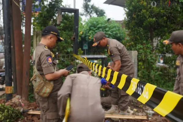 Petugas saat memasang Pol PP line di lokasi galian tanah. (Poskota/Veronica)