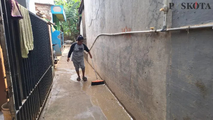 Salah satu warga saat membersihkan lumpur di depan rumahnya di Kampung Lebak, Bekasi Utara, akibat banjir luapan Kali Bekasi, Senin, 11 November 2024. (Poskota/Ihsan)