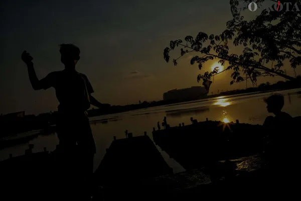 Sejumlah warga saat bermain layang-layang sambil menikmati suasana senja dengan latar belakang Jakarta Internasional Stadium (JIS) di Waduk Cincin, Papanggo, Jakarta Utara, Minggu, 1 Desember 2024. (Poskota/ Ahmad Tri Hawaari)