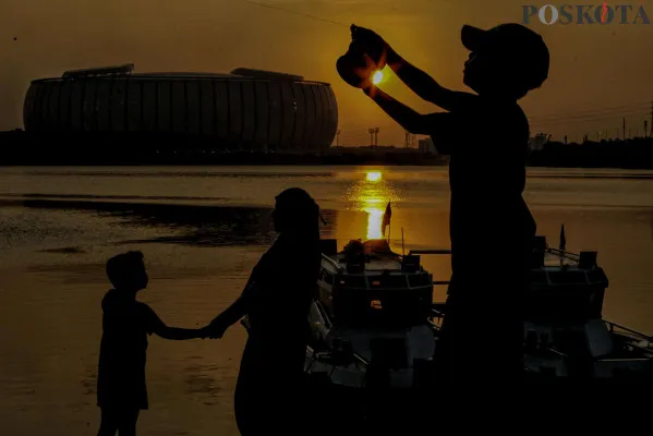Sejumlah warga saat bermain layang-layang sambil menikmati suasana senja dengan latar belakang Jakarta Internasional Stadium (JIS) di Waduk Cincin, Papanggo, Jakarta Utara, Minggu, 1 Desember 2024. (Poskota/ Ahmad Tri Hawaari)