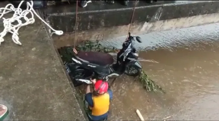 Petugas damkar saat mengevakuasi motor warga yang tercemplung ke aliran Kali Cengkareng Drain. (ist)