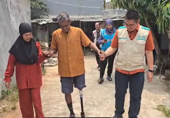 Foto: Manager PLN Unit Pelaksana Pelayanan Pelanggan Pondok Kopi, Ari Tirtaprawita, membantu Ridwan H. Hilabi berjalan dengan kaki palsu.(Dok. PLN)