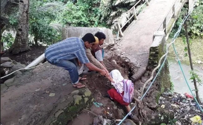 Salah seorang warga saat membantu siswa naik ke jalan usai menyebrang sungai. (Ist).