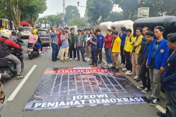 BEM SI membentangkan spanduk bergambar wajah Presiden RI, Joko Widodo (Jokowi) yang terpenjara di dalam sel di depan Gedung KPU RI, Jakarta Pusat poada Jumat (9/2/2024).(Poskota.co.id/Pandi Ramedhan)