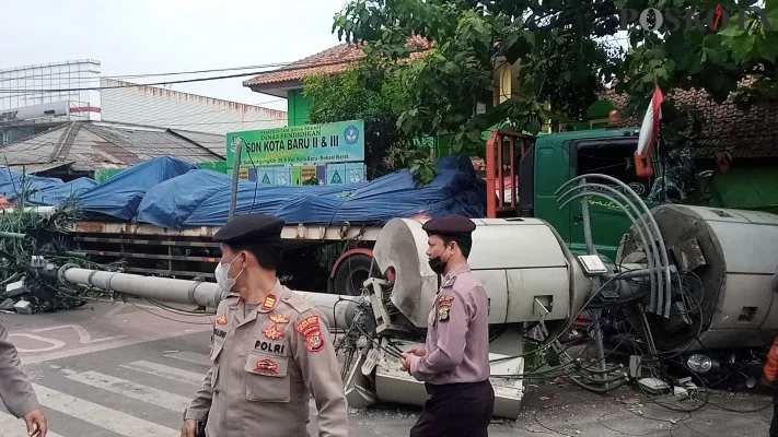 Petugas kepolisian berlalu lalang melintas di depan truk pengangkut besi tabrak tiang provider di jalan Sultan agung depan SDN II dan III Kota Baru Bekasi. (Poskota/Ihsan Fahmi)