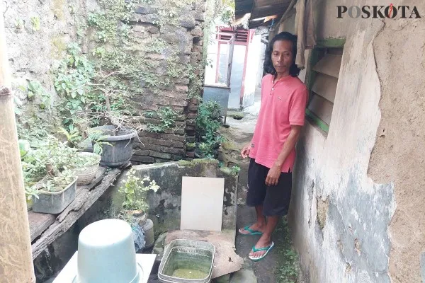 Janim, pria lajang 46 tahun di Kota Serang saat menunjukan toilet terbukanya di gang rumah untuk mandi malam. (Poskota.co.id/Bilal Hardiansyah)