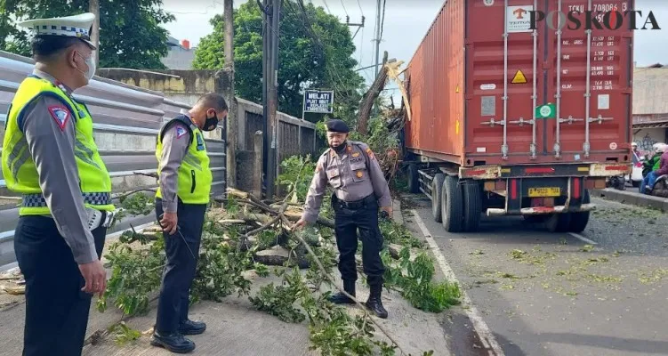 Kanit Lantas Polsek Bojongsari AKP Suharto bersama Kanit Samapta didampingi anggota membantu membersihkan sisa potongan batang pohon yang  ditabrak truk peti kemas.(angga)