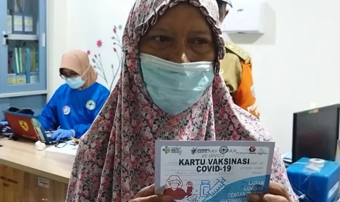 Yanti Susanti (memegang kartu vaksinasi Covid-19) mengantarkan anaknya Dian yang melakukan vaksinasi Covid-19 bagi ODGJ di Puskesmas Kecamatan Ciracas, Selasa (12/10/2021). (Foto/cr02) 