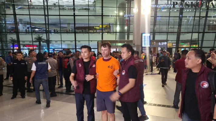 Tampang Roman Nazarenco, WNA Ukraina yang berstatus buronan kasus peredaran narkoba saat dibawa polisi di Bandara Internasional Soekarno-Hatta (Soetta), Kota Tangerang, Minggu, 22 Desember 2024. (Poskota/Pandi Ramedhan)